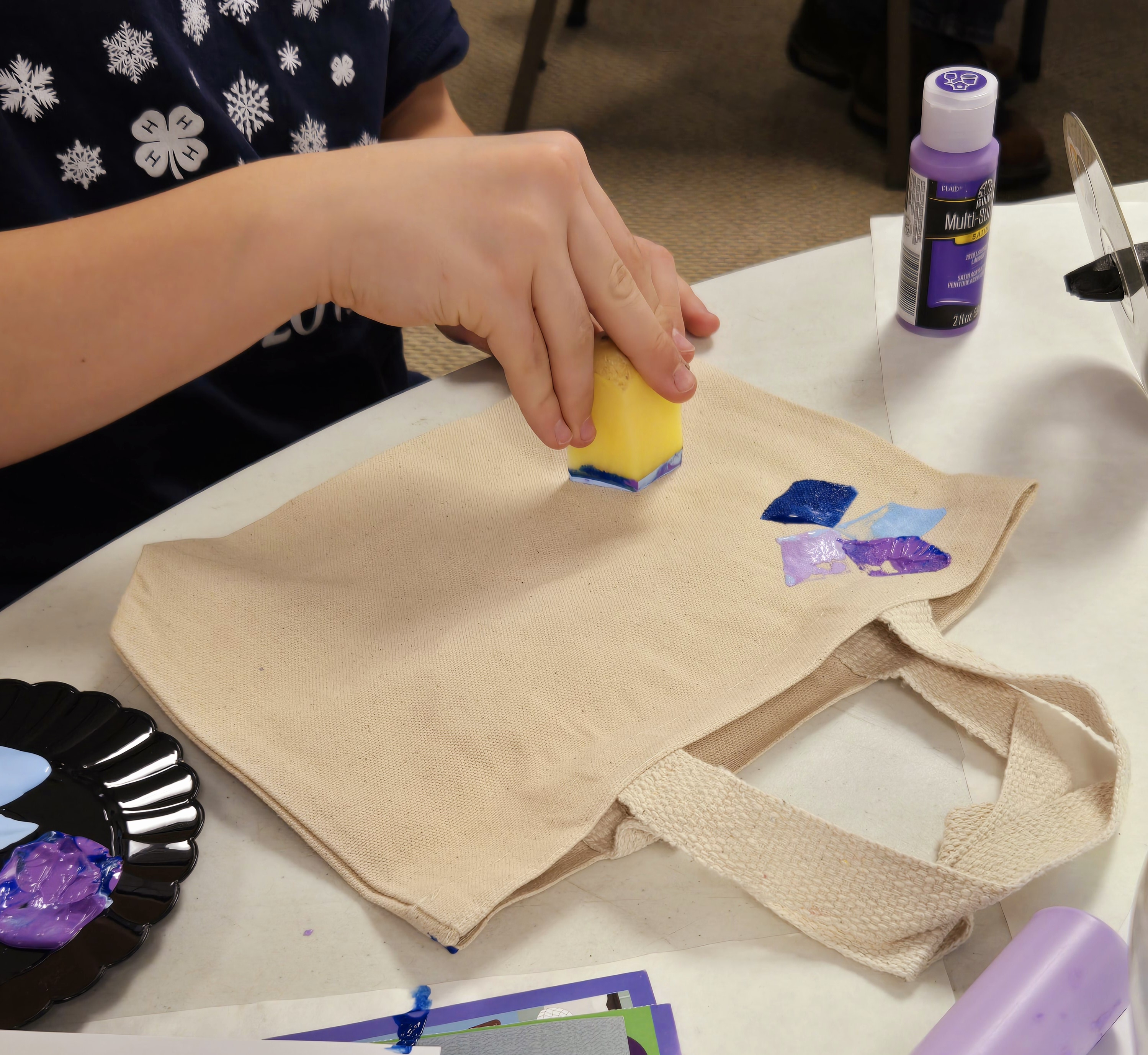 Girl pressing a carved potato dipped in paint onto a bag.